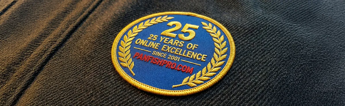 We are honored to announce the commemoration of our twenty-fifth anniversary of online operation. The accompanying image displays an embroidered circular patch affixed to a blazer, inscribed with the text: “25 years of online excellence -Since 2001- Panfishpro.com.” The patch features gold trimming and gold lettering set against a blue background.